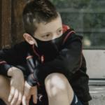 一个戴着面具的白人小男孩坐在台阶上。他看起来像是在等人。