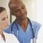 一个穿着蓝色手术服，戴着听诊器的黑人男子和一个穿着白色医院大褂的白人妇女