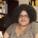 一位黑人妇女坐在笔记本电脑前，一头浓密的自然头发，戴着一副时髦的黑边眼镜