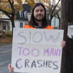 男子举着写着“慢下来，太多车祸”的牌子