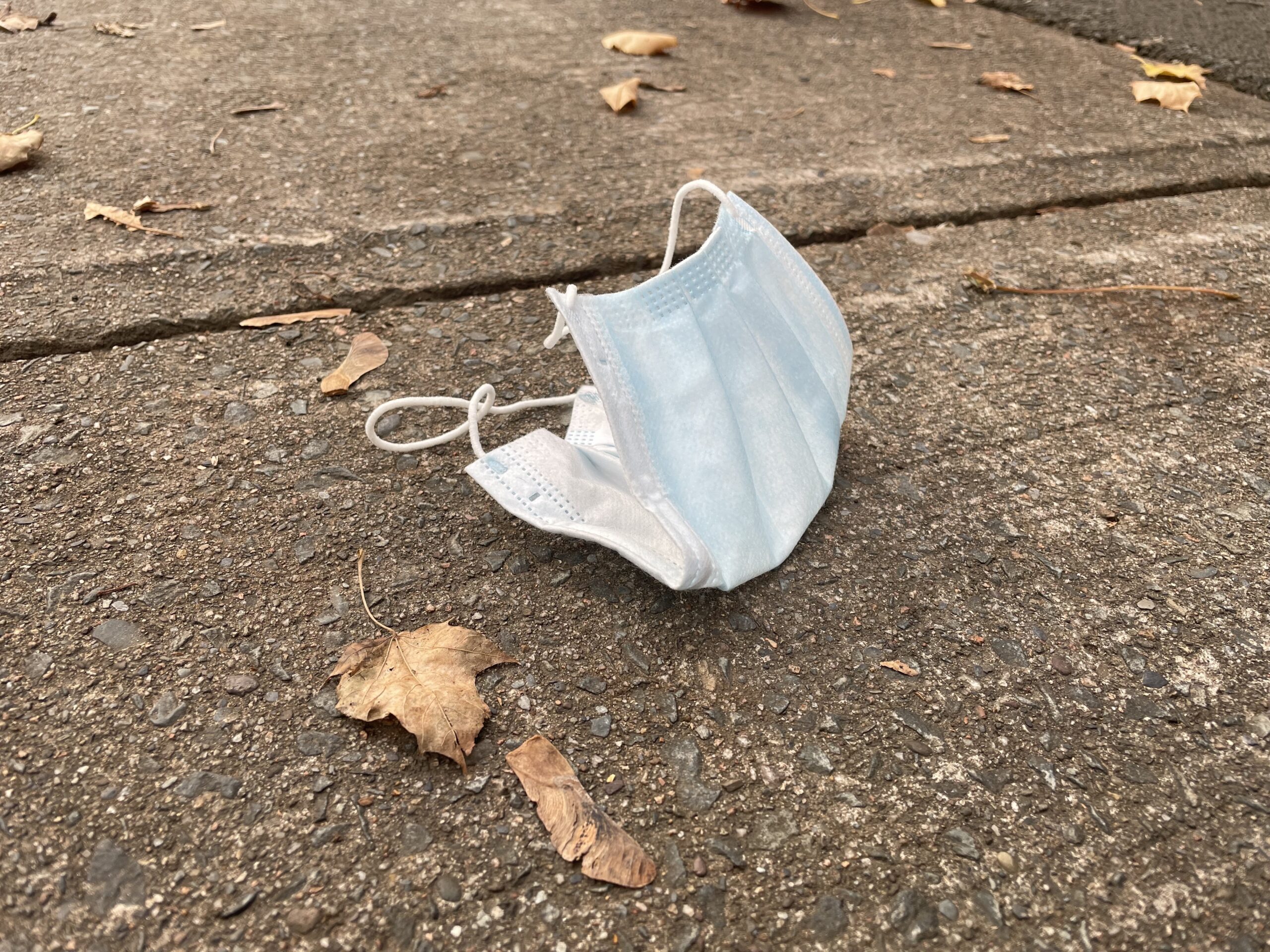 一个浅蓝色的外科口罩散落在人行道上