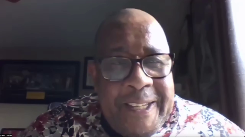 在赔偿和奴隶制的虚拟小组中发言的Cikiah Thomas的屏幕截图。托马斯戴着眼镜和印花衬衫。