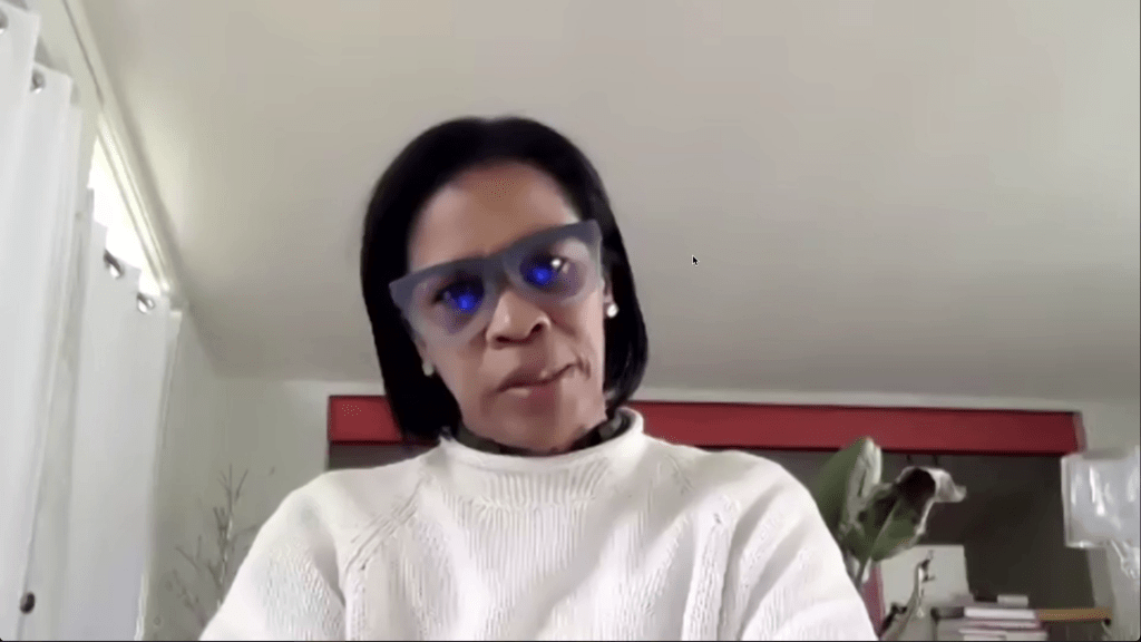 这是一张安德里亚·道格拉斯关于赔偿和奴隶制的讨论的截图。道格拉斯戴着眼镜，穿着白色毛衣。