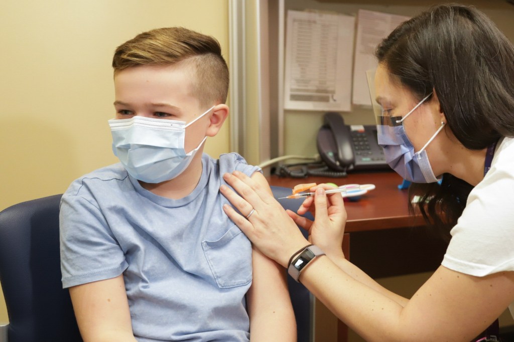 A child wearing a blue shirt is being vaccinated by a nurse wearing a white shirt