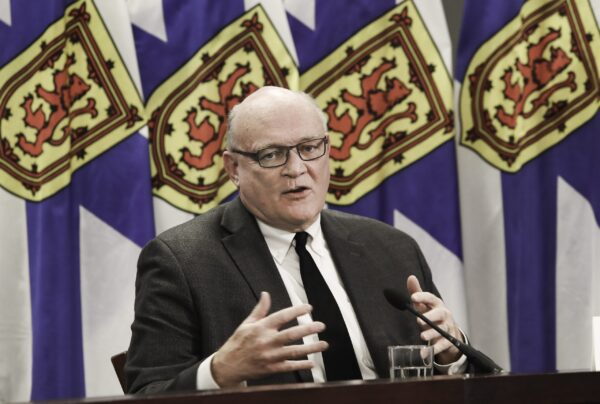 一个男人坐在桌旁用手说话。背景中有新斯科舍省的国旗