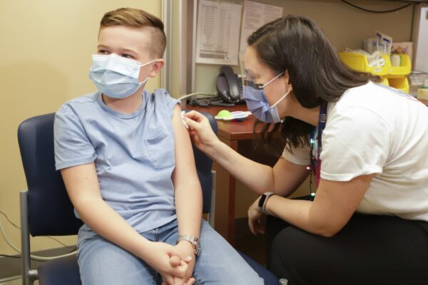 身穿蓝色衬衫的儿童正在接受身穿白色衬衫的护士的接种