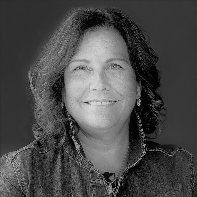 黑白照片中是一名白人女子的头像，她留着齐肩长发，穿着一件开领衬衫，面带友好的微笑。