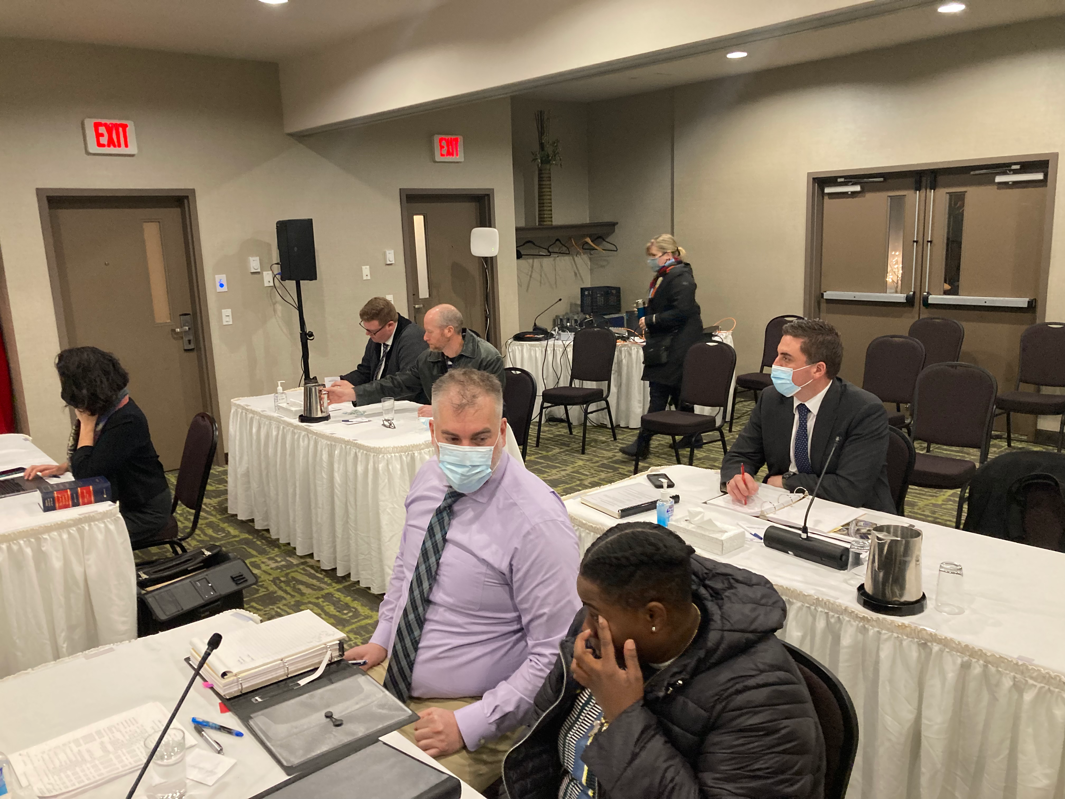 A photo of the room where the appeal hearing is taking place. The room in a Burnside hotel includes several tables where witnesses and lawyers sit. At the table in the foreground is Kayla Borden and her lawyer, Devin Maxwell.