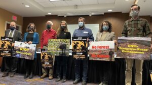 seven protestors hold signs saying no cutting and save wildlife in a hotel conference room following a news conference. They are wearing masks and posing for the camera