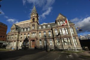 在一个阳光明媚的冬日里，可以看到一座石头建筑。地上没有雪。这座对称的建筑中央有一个高高的尖顶，尖顶上有一个钟，两侧各有两个大天窗。在中央塔楼的每一侧都有一系列的三个较小的天窗。这张照片是从大楼的右边拍摄的。