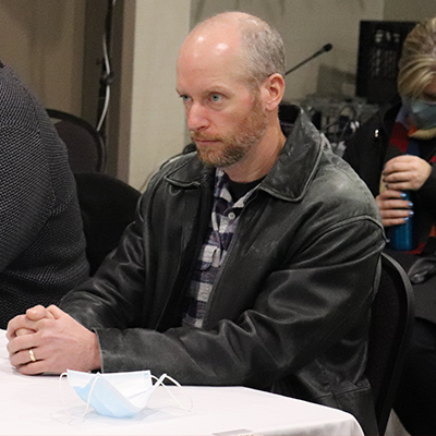 身穿深色皮夹克的白种光头男子热切地望着前方。