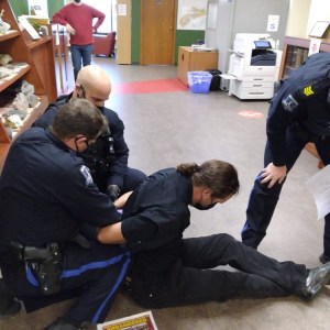 凯文·史密斯被三名哈利法克斯地区警察逮捕。史密斯躺在地板上，两个人在他身后给他戴上手铐。另一间办公室就在史密斯的前面。