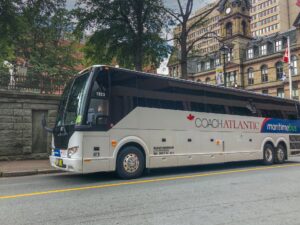 哈利法克斯市政厅前巴林顿街上的海事巴士。这辆公共汽车是白色的，窗户是深色的。车身侧面画有一个标志，上面写着大西洋长途海运巴士。