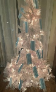 一只10个月大的小猫砸坏了一棵白色圣诞树，圣诞树上装饰着蓝色的一次性口罩。