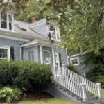 A gabled house with pale blue shingles and white and black trim