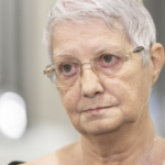 An older white woman with glasses and a short silver pixie haircut looks at someone off camera