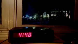 闹钟显示4点48分放在黑暗的窗户旁边。外面只有阴影和圣诞彩灯