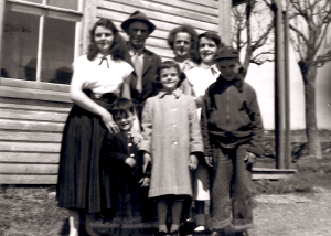 一张老的黑白照片，一家人穿着他们最好的衣服站在他们的家外面。