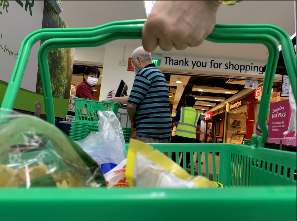 在杂货店收银台排队付款时，一个人的手放在绿色杂货篮子上。