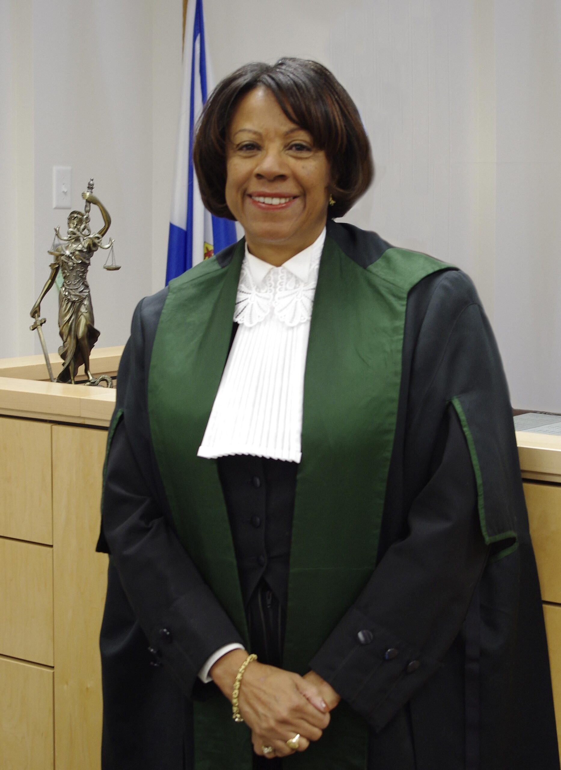 身着黑色长袍的黑人女法官在法庭长凳前对着镜头微笑。
