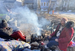 在居民区的一个小公园里，两个人穿着全套冬装坐在那里，他们之间燃起了熊熊的炉火。他们是