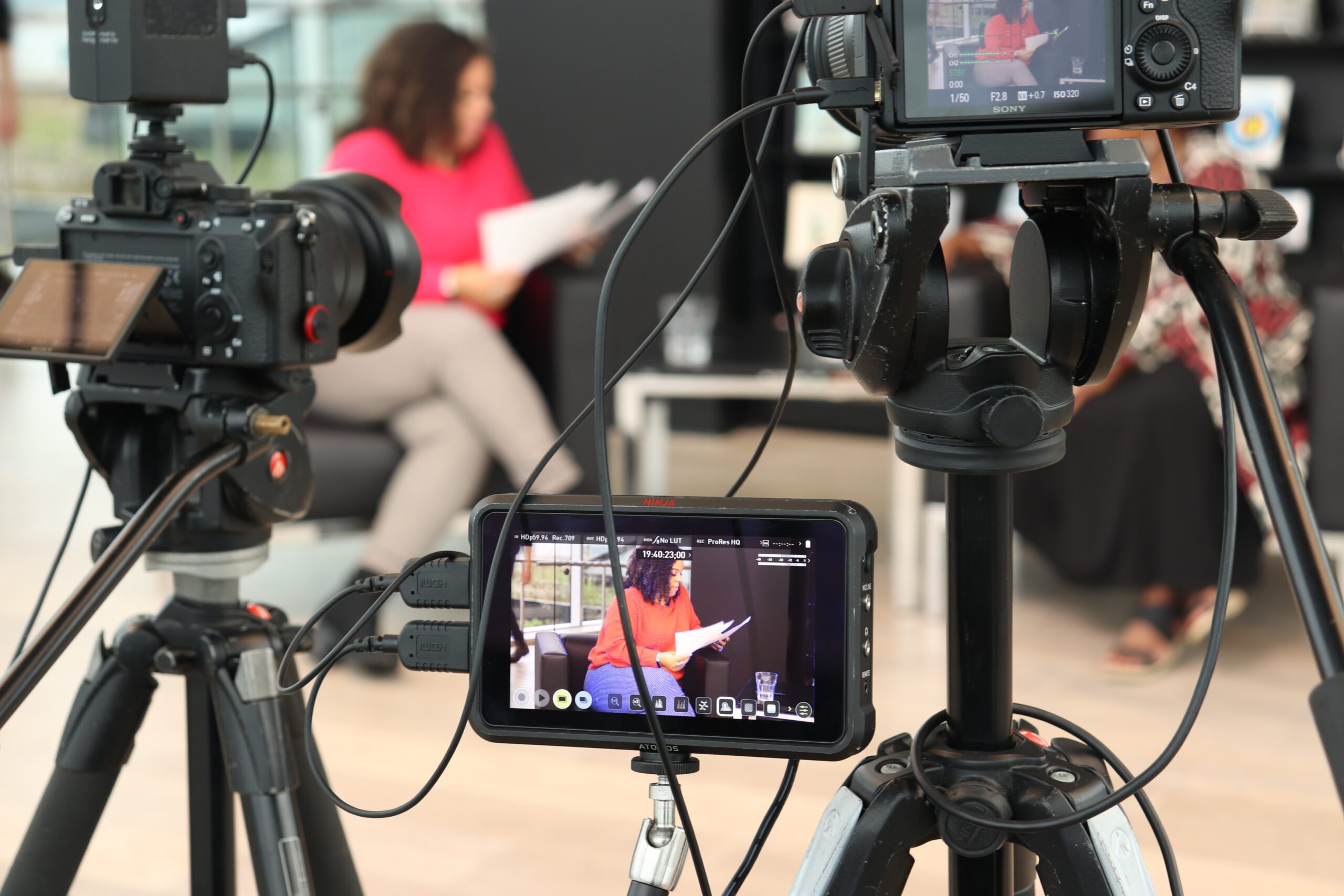 监控器拍摄到一位穿着粉红色衬衫的黑人女士坐在黑色扶手椅上复习笔记。