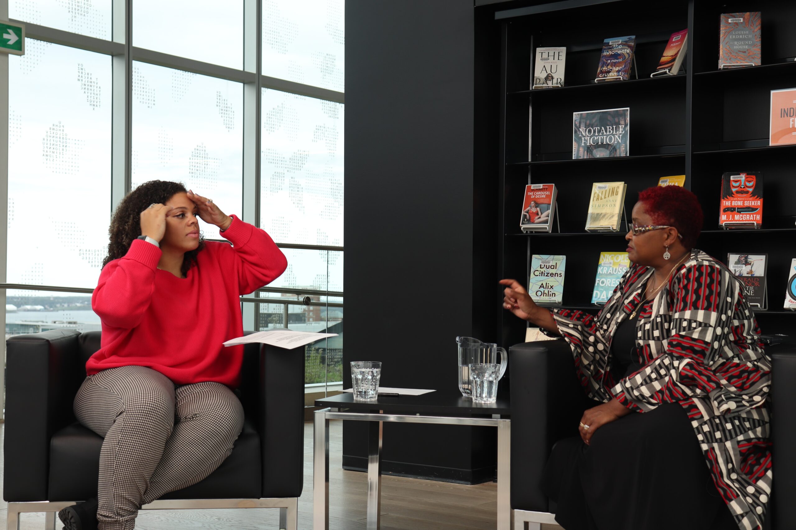 两位黑人女士面对面坐在黑色扶手椅上，中间放着一张咖啡桌