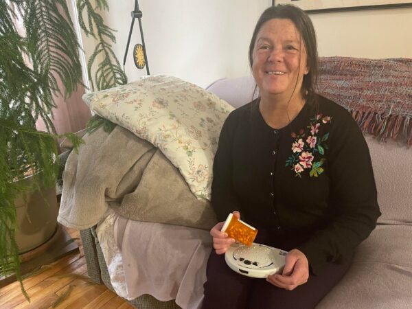 Milena坐在沙发上演示如何使用ScripTalk，这是一种用于扫描处方瓶上的代码并大声读出标签上的说明的手持设备。