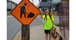 米莱娜·卡扎纳维希乌斯(Milena Khazanavicius)面带微笑，竖起中指，指着一个巨大的橙色警告标志的尖角。她的导盲犬路易斯看起来也不怎么高兴。