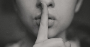 一张黑白特写照片，一个人用手指捂住嘴，做出嘘的手势