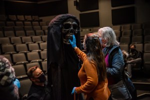 一名戴着蓝色乳胶手套的妇女伸手去摸一个剧院演出的木偶。木偶正被木偶师控制着。