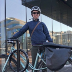 戴着头盔、穿着蓝色风衣的白人妇女吉莉安·班菲尔德(Jillian Banfield)在中央图书馆外骑着自行车