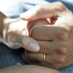 一个男人带着结婚戒指的手握着一个女人的手的特写。他的手是浅棕色的，她的手是苍白的。