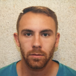 一个白色的男人，浅棕色的头发和胡子，用他的回到墙上，看起来很聪明地看着镜头