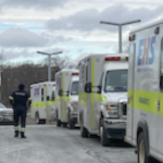 一名护理人员走在一排等候的救护车旁边