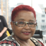 巴布·汉密尔顿-辛奇医生，一位留着红色短发，戴着时髦的黑红灰眼镜的黑人妇女。