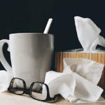 床头柜上有一个杯子，一盒纸巾和一副老花镜