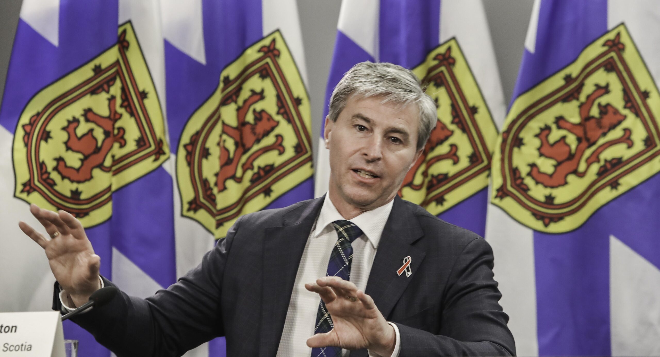 a man gesturing in front of Nova Scotia flags
