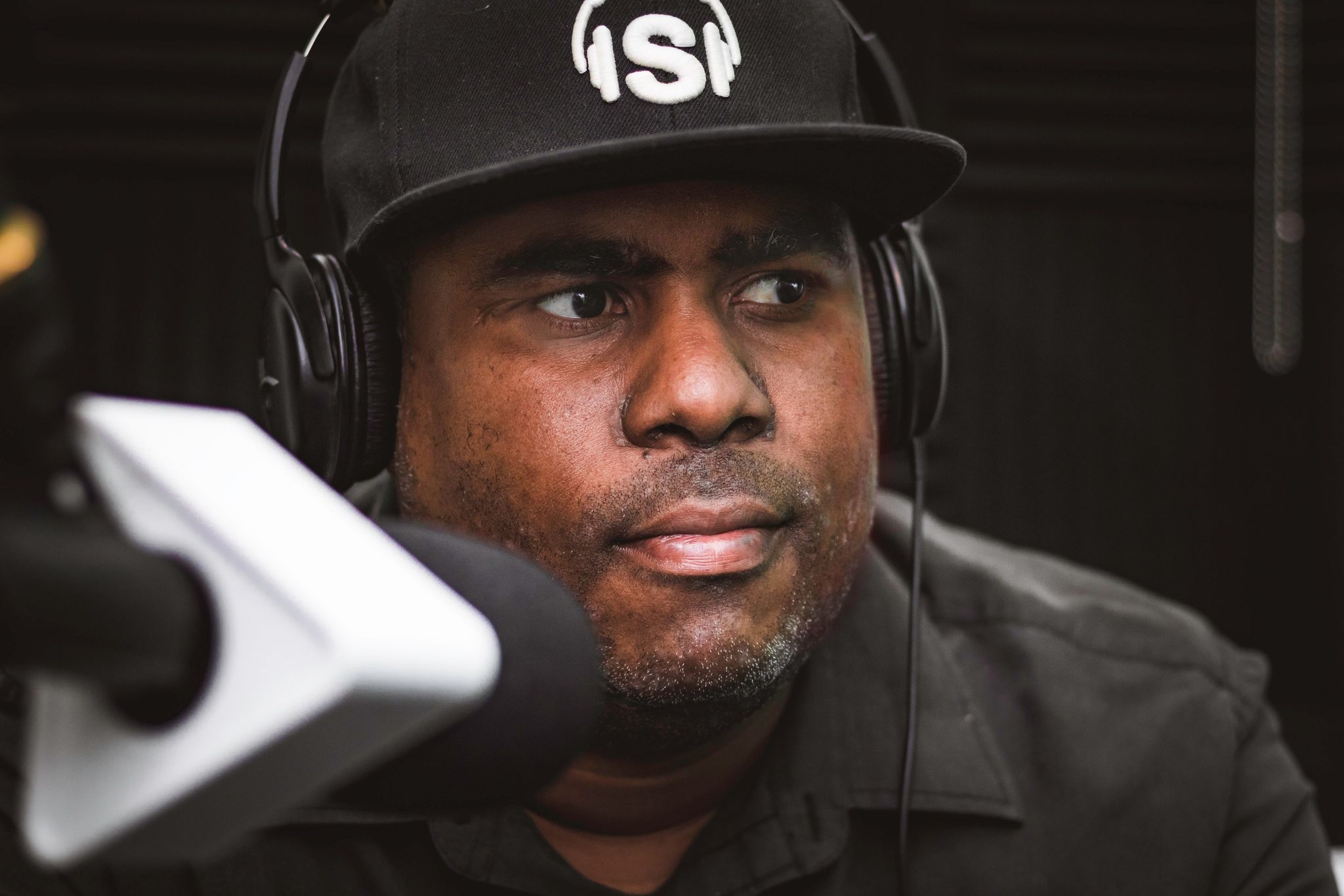 特写黑人男子黑色衬衫和黑色棒球帽，戴着黑色耳机在麦克风前