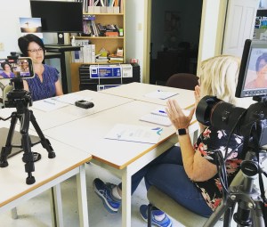 一个金发女郎站在摄影机后面采访坐在桌旁的另一个女人。