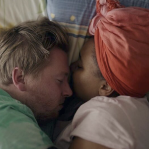 电影剧照，一个白人男人和一个黑人女人在床上相互依偎