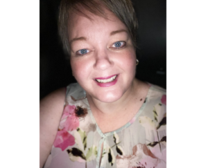 一名留着短发、身穿米色印花上衣的女子微笑着微微歪着头，对着镜头微笑。