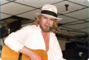 A man in a white shirt and hat playing a guitar
