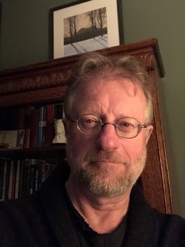 一个戴着眼镜、留着胡子的中年白人男子的头像，直直地盯着摄像机