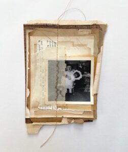 一种由发黄的纸层叠而成的拼贴画，有些是透明的，有些是打印的文字，有些是深棕色的纸或织物。有一张黑白照片，一个白人小女孩抱着一个几乎和她一样大的娃娃，整个东西是用粗糙的棕色线缝在一起的。