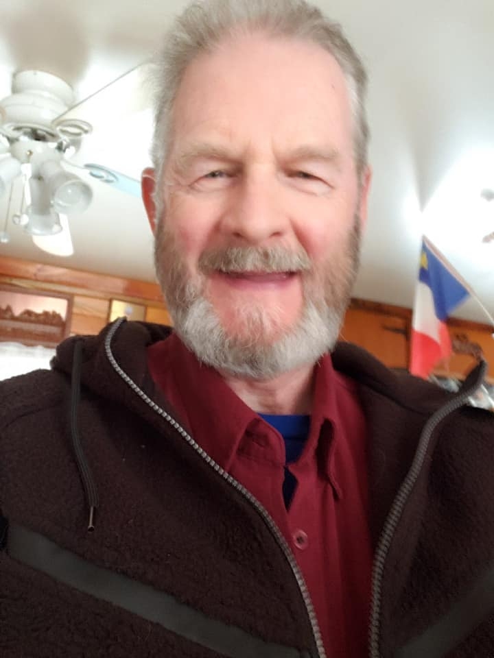 一个白胡子白头发的白人男人穿着酒红色衬衫和深色毛衣