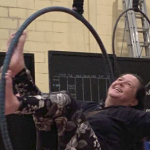 一名白人女子坐在体育馆天花板上悬挂的铁环内大笑