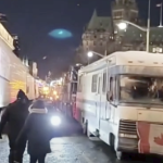 A winnebago with a Canadian flage draped on the front blocks a street in Ottawa at night