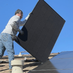 一个人在屋顶上安装太阳能电池板。他没有使用适当的保护齿轮。这张照片在新斯科舍省没有拍摄，我们关心这样的东西。