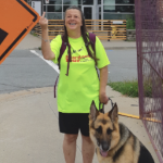 一名身穿霓虹灯绿色T恤的白人女子对着人行道上的警告标志竖起中指。她的导盲犬四处张望。